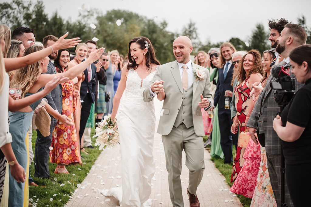 Bride and groom walking through confetti smiling to guests